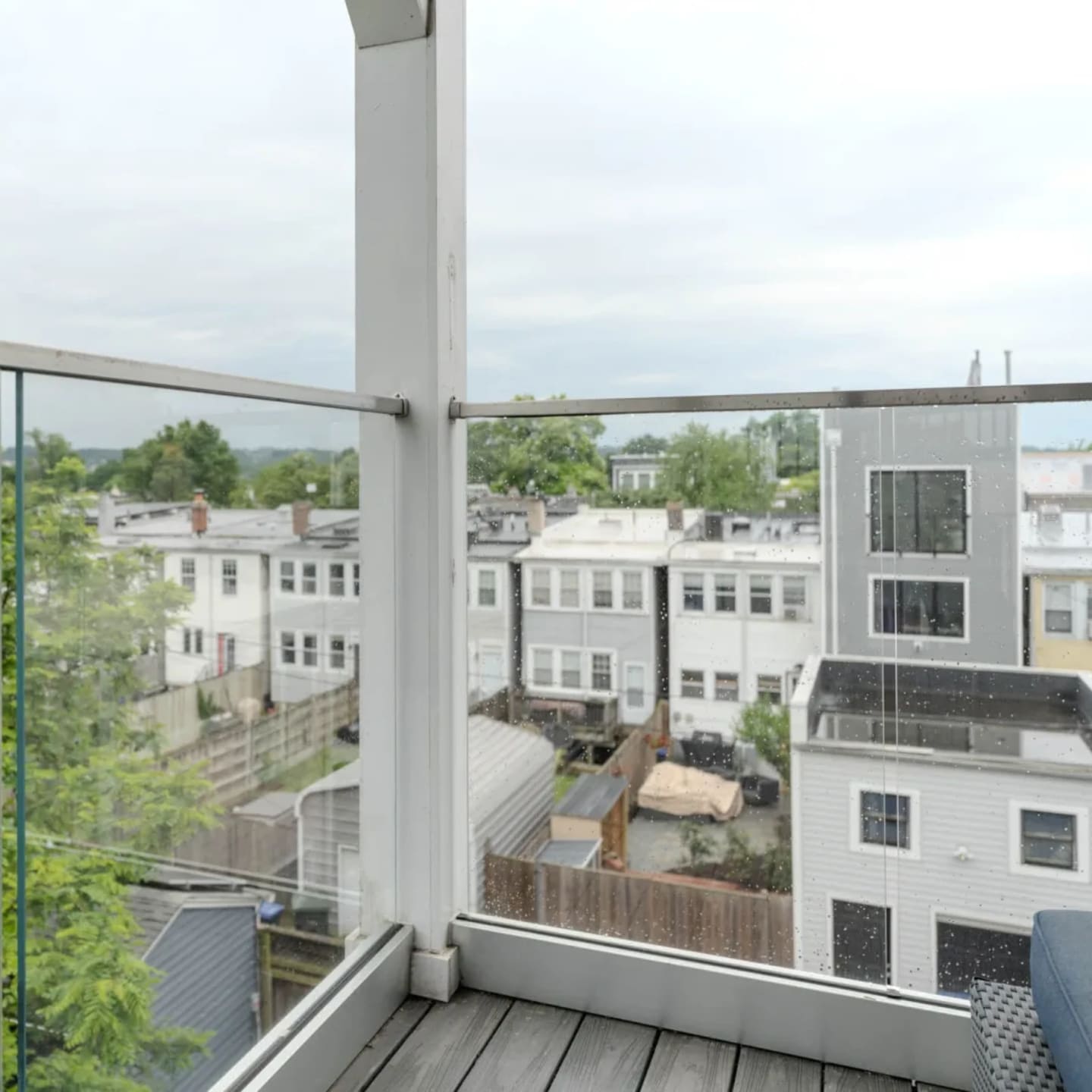Outdoor balcony with frameless glass railing looking over rooftops and treetops