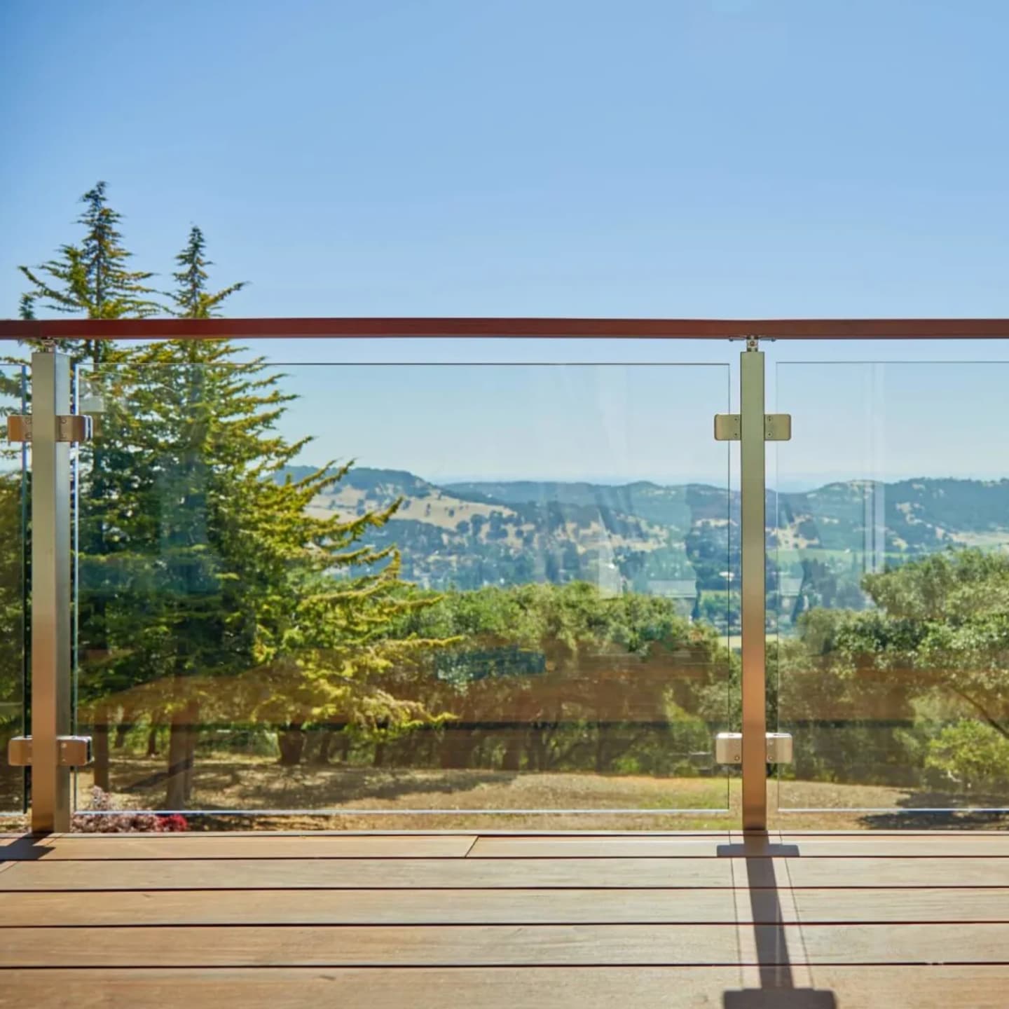 Wood-capped glass railing framing a broad view of hills and treetops
