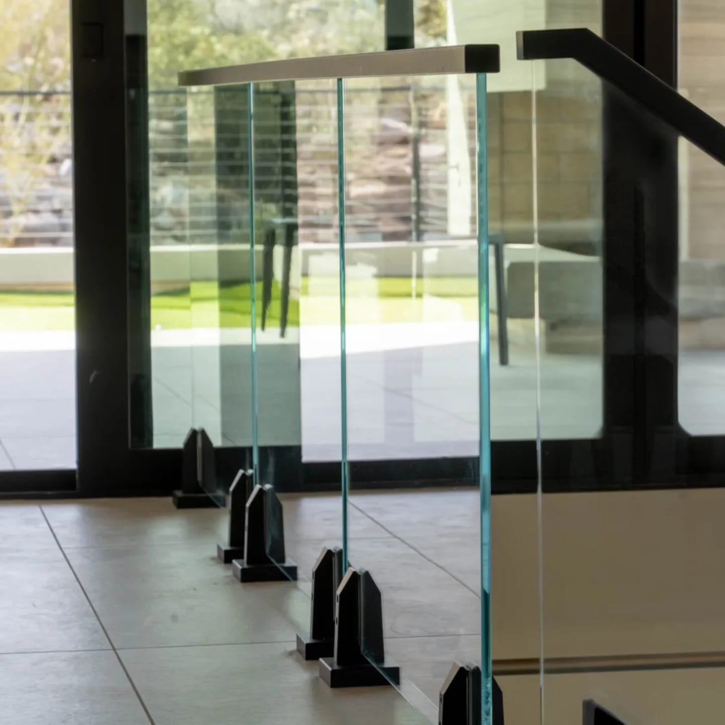 Glass panels on black base clamps at a landing facing tall windows and desert boulders