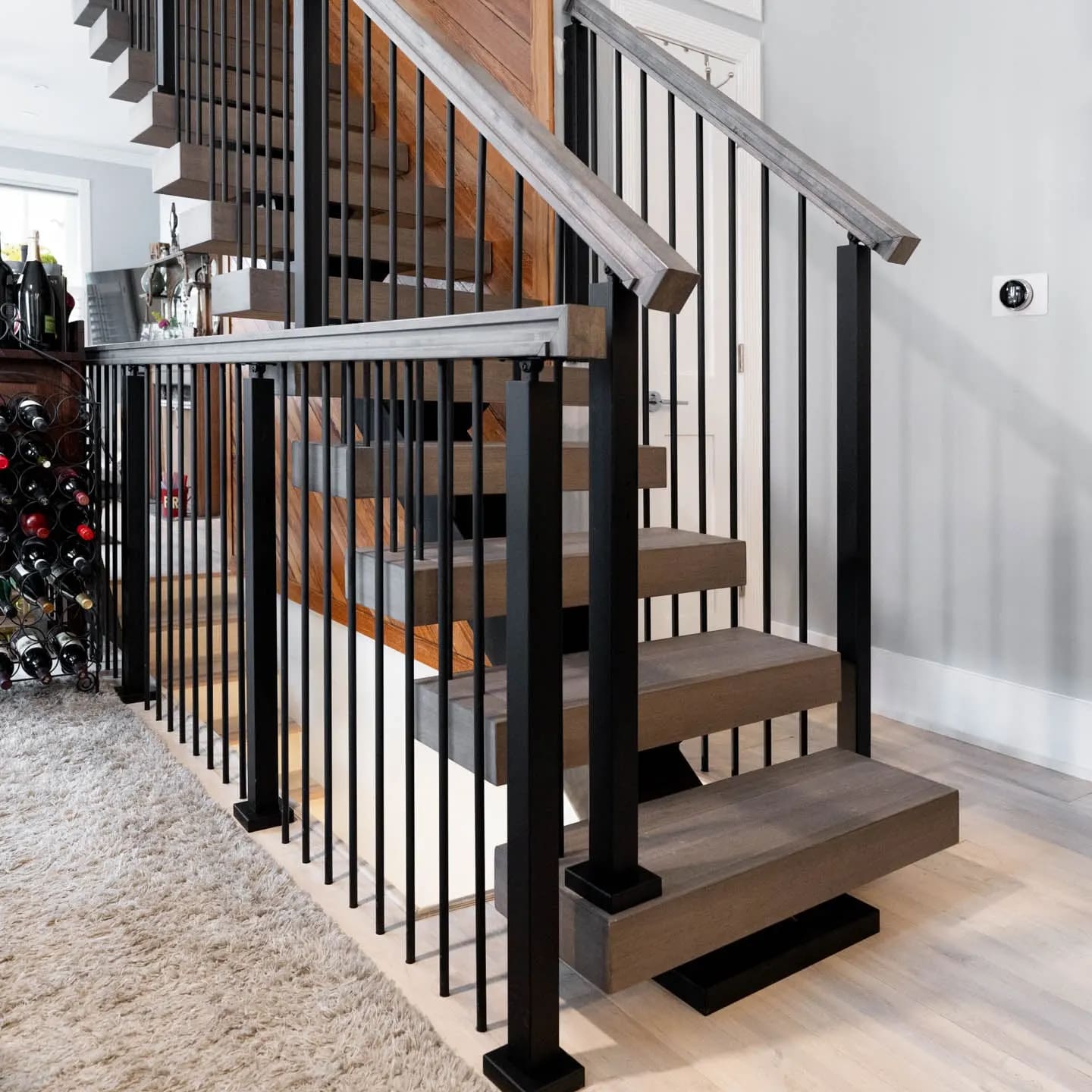 Stair with vertical black rod infill and gray treads beside a plank wall