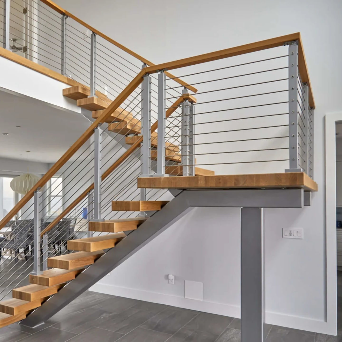 Switchback floating stair with brushed silver stringer, rod infill and a wood top rail