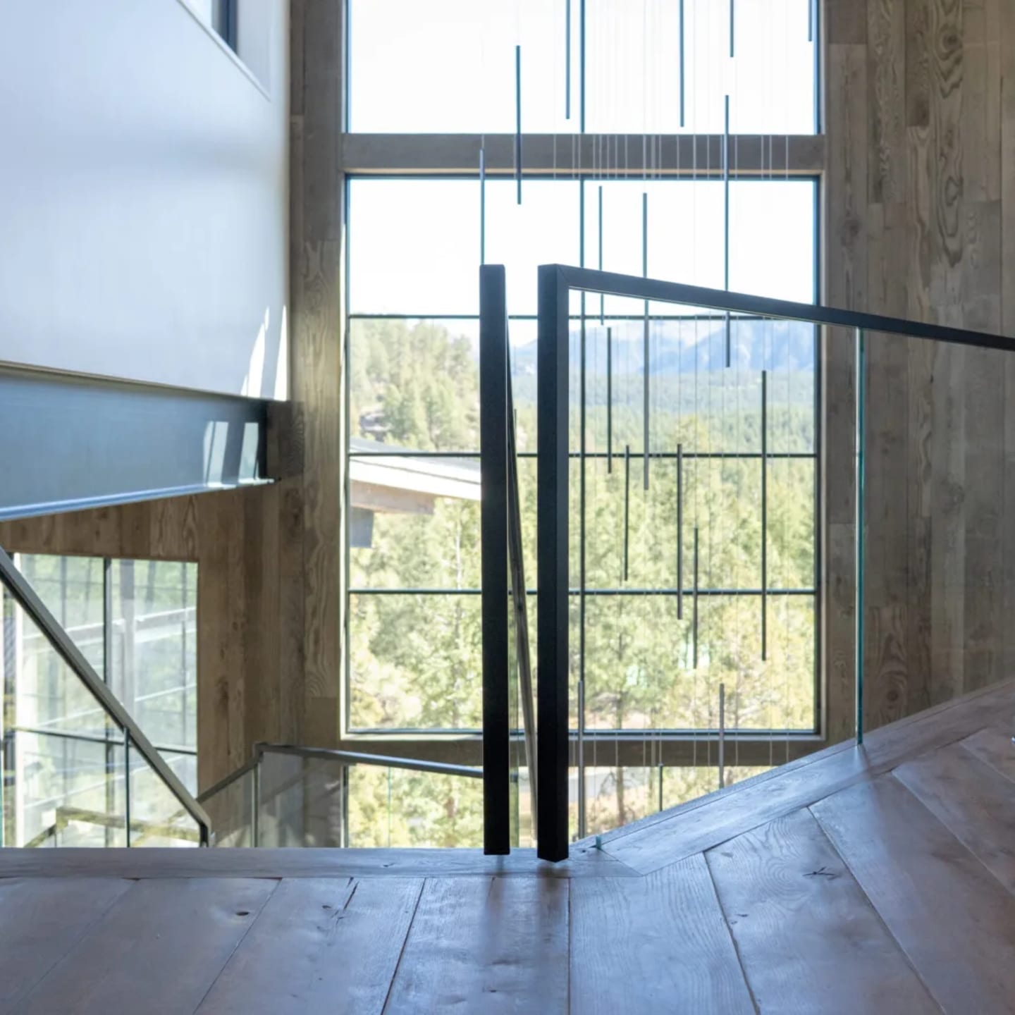 Upper landing glass railing overlooking a switchback stair and wooded valley beyond tall windows