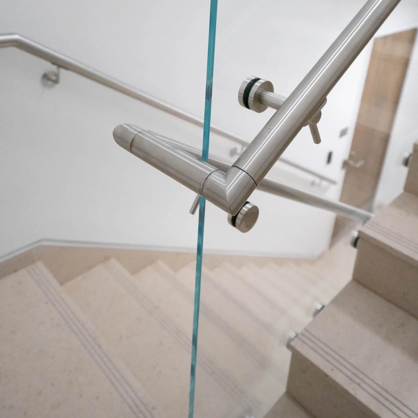 Round stainless handrail turning at a landing where it clamps through glass