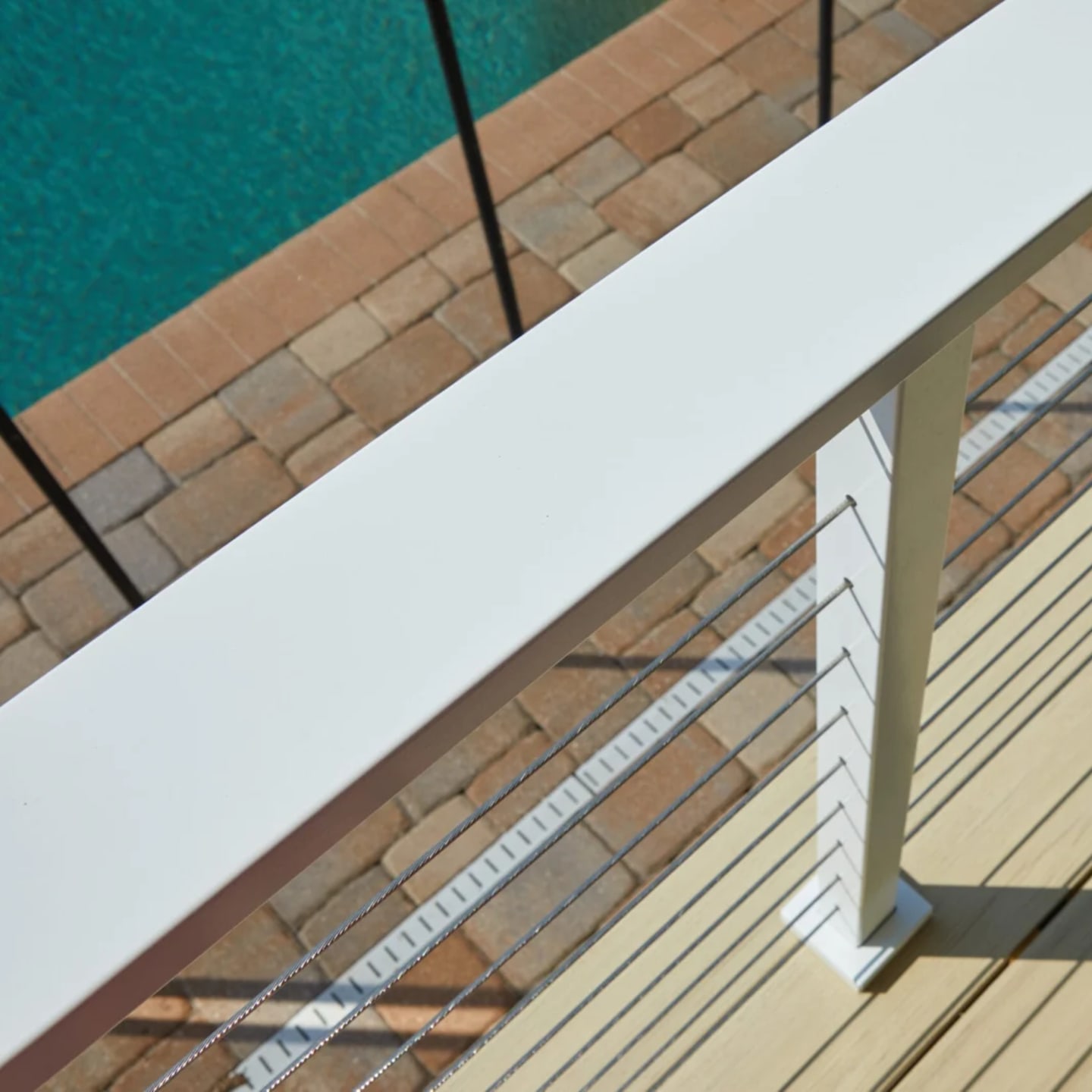 Wide flat white top rail angled above a poolside deck and brick pavers