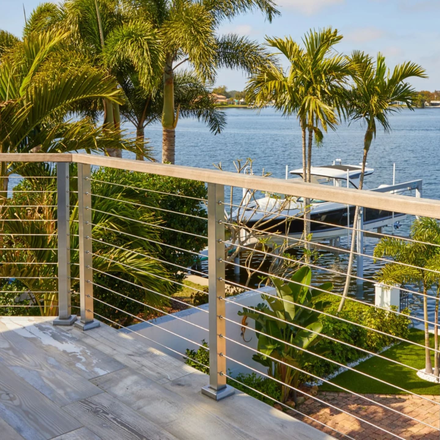 Cable railing borders a waterfront deck lined with palms on a canal