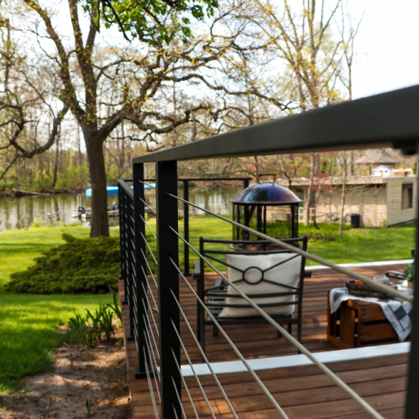 Black cable railing wrapping a deck of lounge chairs above a lawn and creek