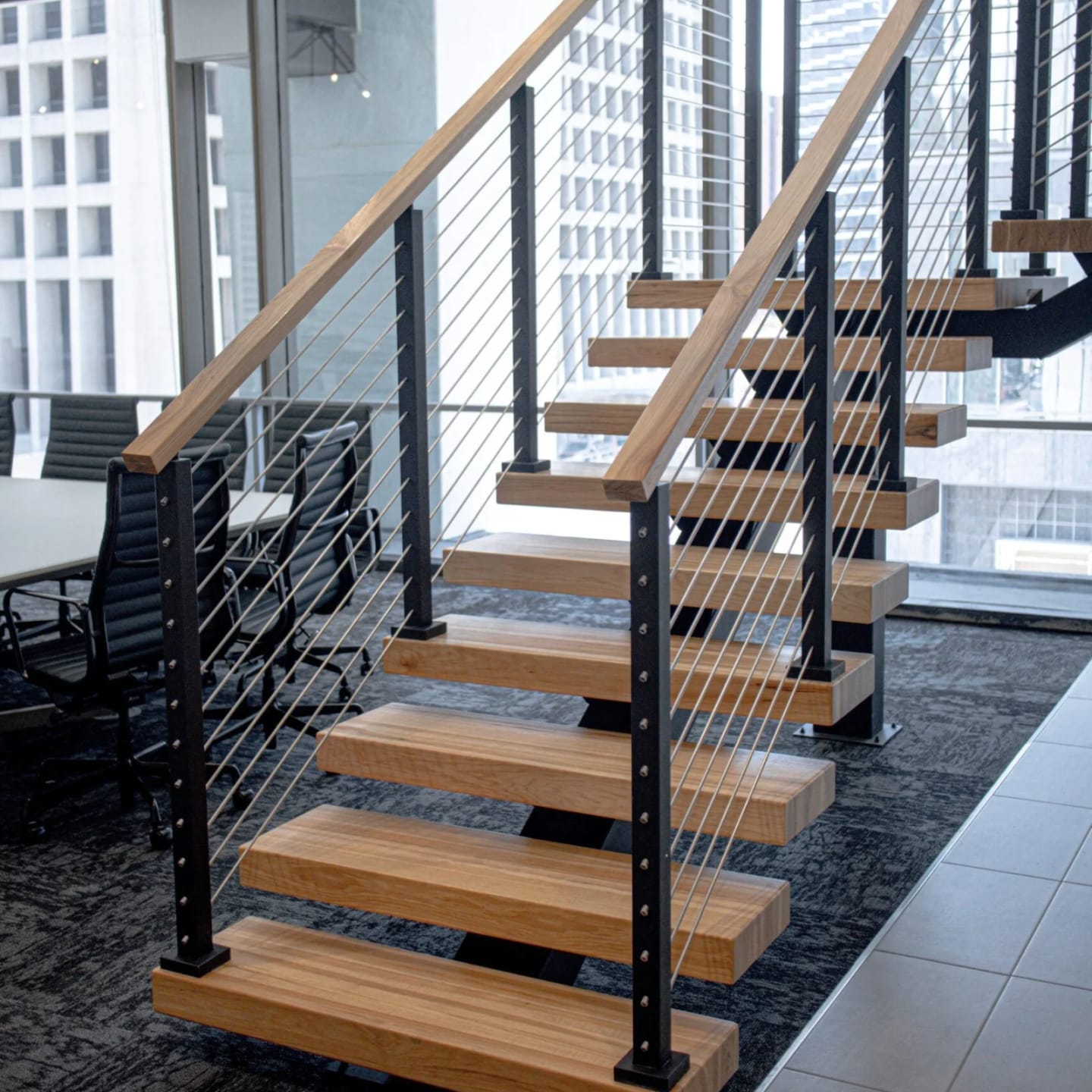 Office stair with light treads and cable railing beside a glass conference room and city towers
