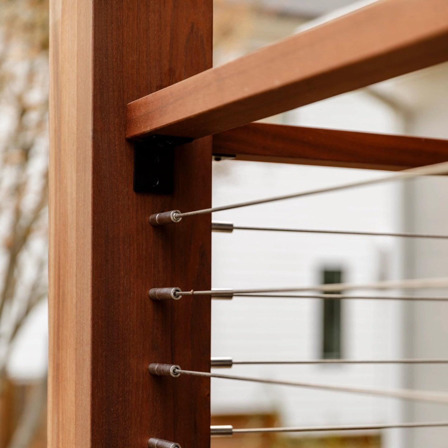 Stainless cables terminating in a warm-toned wood post beside white siding