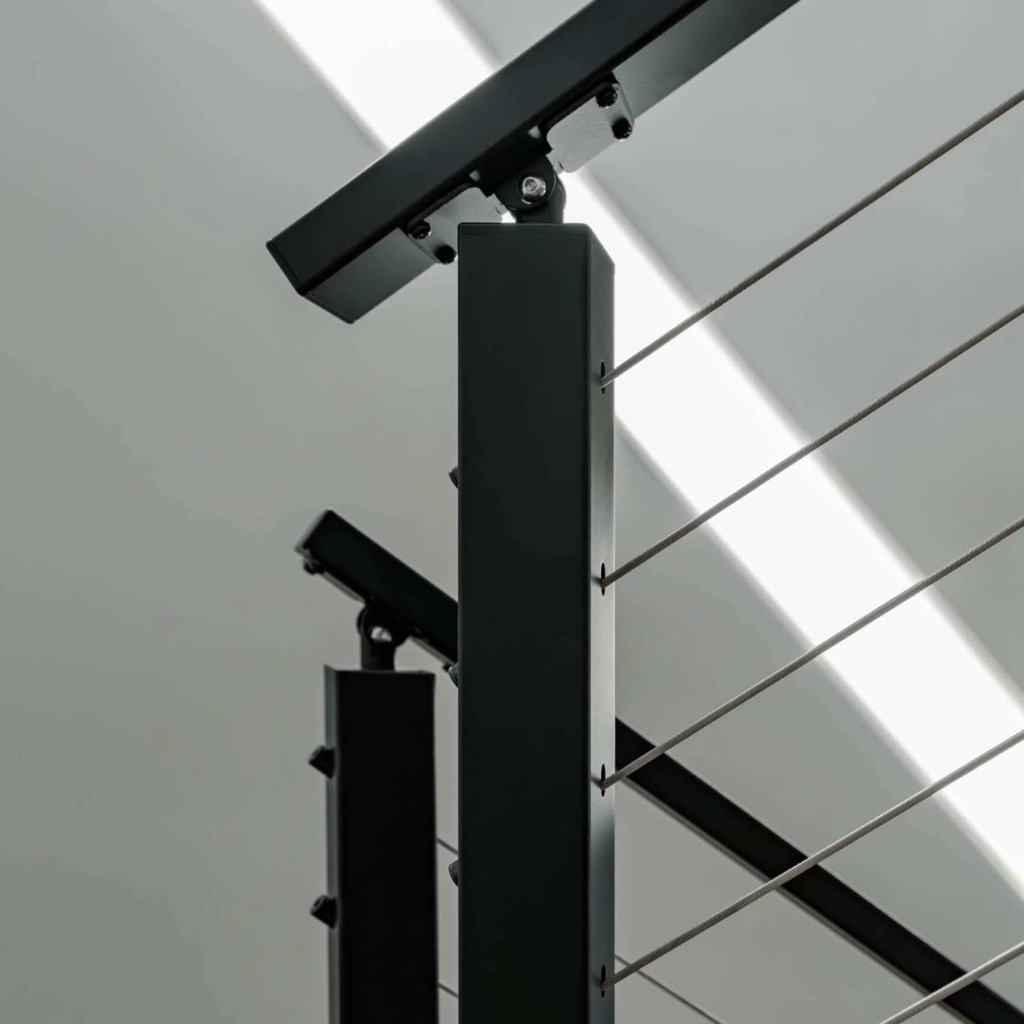 Sunlight across a black top rail and post corner above tight cable runs