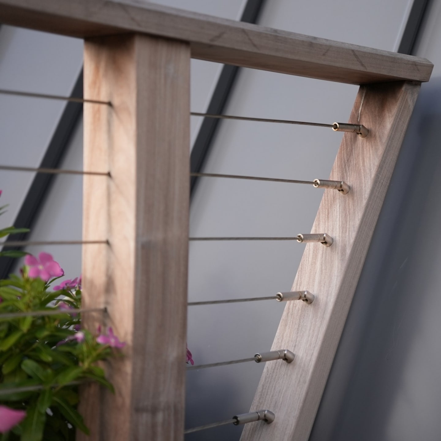DriveTite angle fittings tension stainless cable into a weathered wood stair post beneath a wood cap rail.