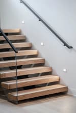 Thick white oak floating treads with a glass railing and a black metal wall-mounted handrail that returns into the wall.