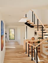White oak floating stair on a black stringer with cable railing and oak handrail beside a bright hallway.