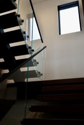 Walnut treads on a black stringer with frameless glass secured by black standoff pins under a skylight.