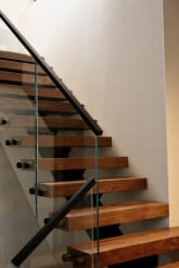 Walnut floating treads rise along a textured white wall with frameless glass and a black handrail.