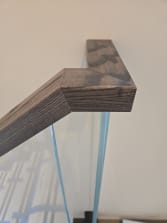 Close view of a weathered oak handrail mitered on top of frameless glass