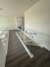 Frameless glass in a white base shoe with a slim cap and a glass-mounted handrail follows a dark-plank stair down from an upper hall.