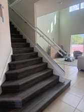 A dark-plank stair rises between a white wall handrail and a frameless glass guard with a glass-mounted handrail.