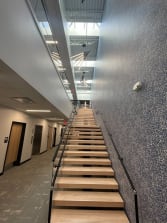 Long oak floating stair with glass railing and black handrail in a commercial office atrium.