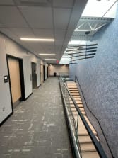 View down a long oak floating stair with glass railing alongside an office corridor.