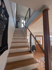 Black cable railing posts with a stained wood handrail follow a white-riser oak stair in a bright home with pale blue walls.