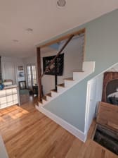 Black cable railing posts with a stained wood handrail follow a white-riser oak stair in a bright home with pale blue walls.