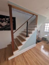 Black cable railing posts with a stained wood handrail follow a white-riser oak stair in a bright home with pale blue walls.