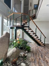 A green-stringer FLIGHT stair with wood treads and matching cable railing rises to a landing over an indoor rock garden.