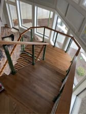Looking down on a wood landing wrapped in green cable railing with a wood cap.