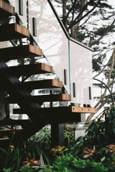 Black exterior FLIGHT Mono stair with slatted wood treads and frameless glass rising through lush greenery.