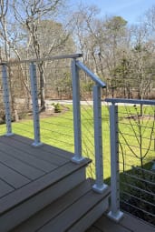 White-post cable railing with a silver top rail wraps composite deck stairs above a green lawn