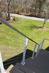 Cable railing with white posts follows composite steps down to a sunny lawn