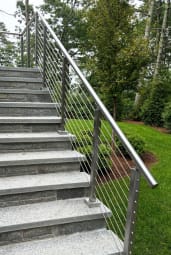 Brushed stainless posts with a 2-inch round handrail and cable infill climbing a long granite garden stair.