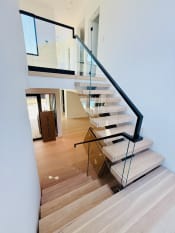 Looking down an oak floating stair with frameless glass and a black flat handrail.