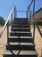 Black cable railing on both sides of composite stairs rising to a deck