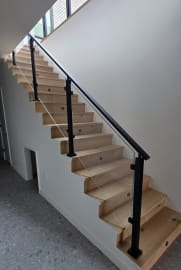 Black post cable railing climbs a straight oak stair over a terrazzo floor