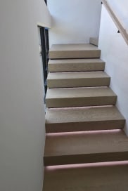 Looking up an oak stair with LED tread lighting and a wall-mounted handrail