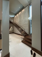 Walnut floating treads cantilevered from a stacked-stone wall with frameless glass and a wood handrail