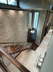 Looking down a walnut floating stair with glass railing beside a stacked-stone wall