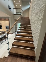 Walnut floating treads rise along a stone wall with glass railing and wood handrail toward a loft