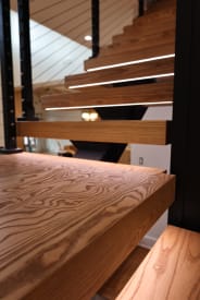 Close view of thick ash floating treads with LED lighting and black cable railing