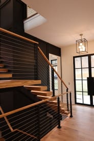 Ash FLIGHT Mono switchback with black cable railing and ash handrail beside a black paneled wall
