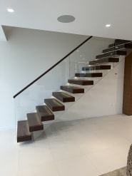 Walnut cantilever treads float off a white wall with a full-height glass railing and dark wood handrail