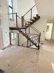 Switchback walnut floating stair with black-post cable railing and wood handrail