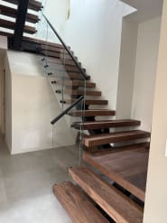 A walnut FLIGHT stair turns at a landing with frameless glass on black standoffs and a black handrail.