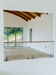 Frameless glass on talon spigots with a wood cap rail overlooks a bright room with a curved wood ceiling