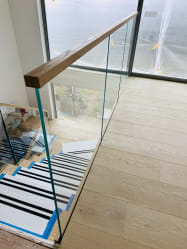Frameless glass panel with a wood cap rail runs along a stair opening above protected treads