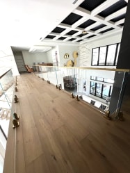 Frameless glass on brass talon spigots runs along an upper-floor balcony under a coffered ceiling