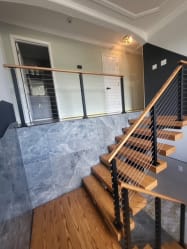 Red oak floating stair with black-post cable railing and wood handrail climbing past a marble wall