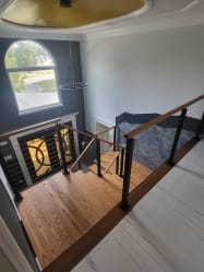 Oak landing and black cable railing seen from above in a two-story foyer with an arched window