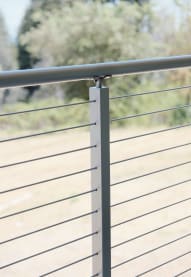 Close view of a silver cable post with round top rail and stainless cables against a field.
